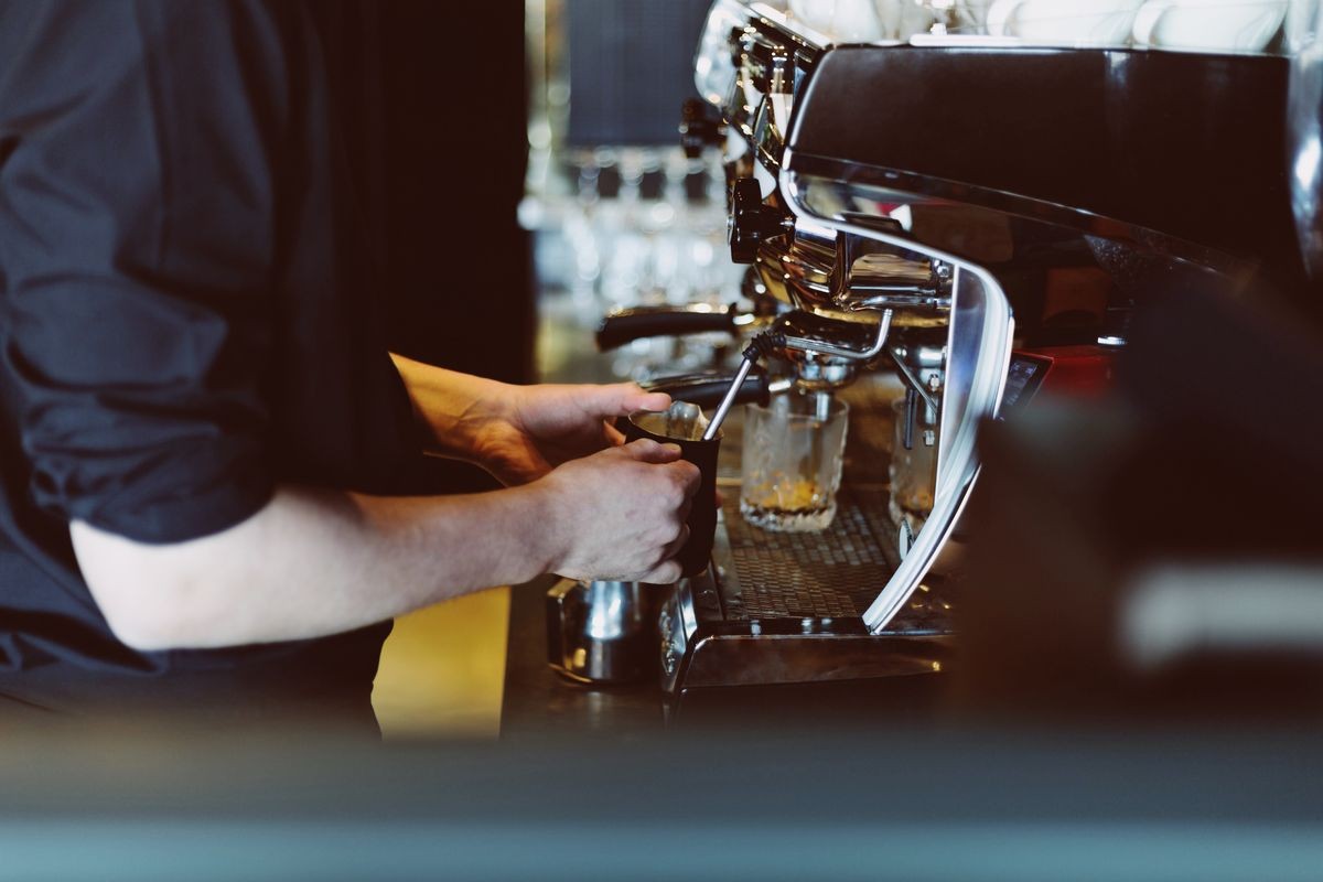 Close up of hands of barman making hot milk for espresso using coffee machine in cafe. Blurred background. Film effect.